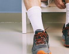 A man leans over to adjust his socks. He is sitting in a white chair while wearing running shoes