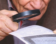 older white man using a magnifying glass to read a piece of paper