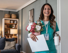 A homecare provider smiling while holding a vase of flowers
