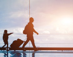 A family of three walking through an airport with their luggage as the sunrise shines in the background.