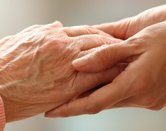 An up-close image of two people clasping hands. One set of hands is elderly and one set is a younger adults. 