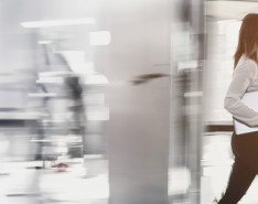 A woman holding a large notepad walking through a blurred office background.