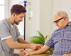 A male caregiver is aiding an older man in home infusion
