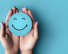 An image of hand against a blue background holding a blue circle smiley face