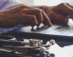 Stethoscope and hands on a computer keyboard 