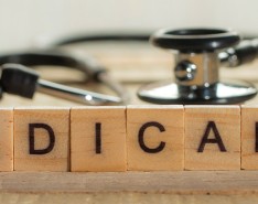 Scrabble pieces spelling out "Medicare" sit on a table, standing up, with a stethoscope behind them. 