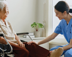 A nurse sits with an elderly patient in a wheelchair.