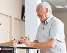 A front of desk person discussing paperwork with an older male patient