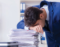 A burnt out employee leaning over a stack of papers