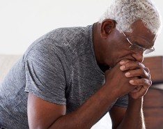 older Black man sits with his chin on his hands looking worried