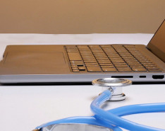 An open laptop sitting on a table next to a stethoscope.