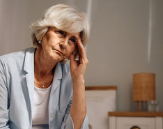 An elderly woman sitting with her hand up to her temple