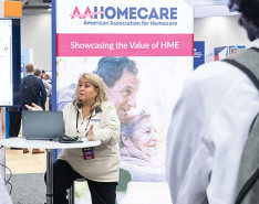 A speaker making a lecture at Medtrade in front of an AAHomecare sign