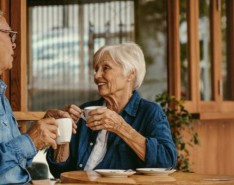 An elderly couple sits at the table drinking coffee and smiling