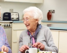 Two elderly women sit and laugh while enjoying their lunch.