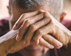 An elderly person with their hands crossed in front of their face