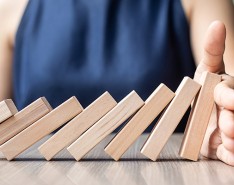 A row of blocks falling on one another in a domino fashion, but someone's hand has stopped them from hitting the last two blocks. 