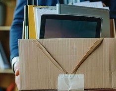 A man in a blue suit holds a brown box filled with office supplies.