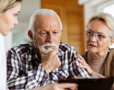 Husband and wife sit with a caregiver looking at a care plan