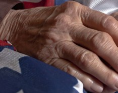 An elderly person's hands clasped over an American flag. 