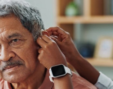 A woman helps an older man adjust his hearing aid