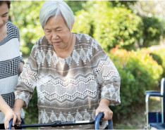 A younger caregiver helping her elderly patient with a walker