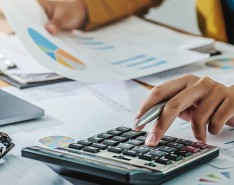 black female hand looks at pie chart and punches numbers into calculator