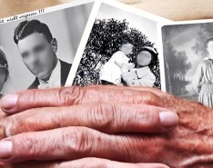 Two elderly hands hold old photographs with the faces blurred out.