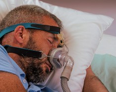 A man sleeps on a pillow with a sleep apnea mask on his face.