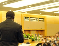 A man speaking at a podium to a room full of people