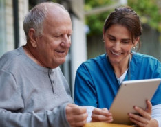 an older man in a wheelchair with a homecare care coordinator looking at an ipad outside