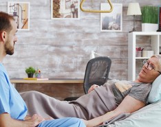 A patient lays in her home hospital bed talking to her caregiver.