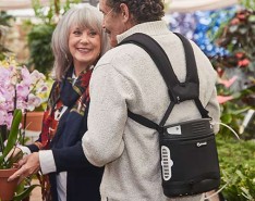 Two older people in a flower market, one is wearing a portable oxygen concentrator
