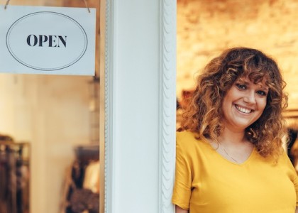 A woman stands in the doors of a boutique that has an "open" sign on the door. 