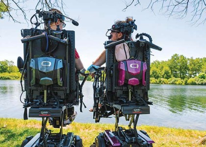 Two people sitting in medical assist chairs by a sunny lake