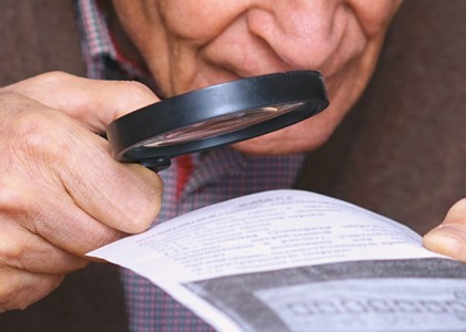older white man using a magnifying glass to read a piece of paper