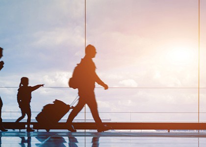 A family of three walking through an airport with their luggage as the sunrise shines in the background.