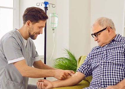 A male caregiver is aiding an older man in home infusion