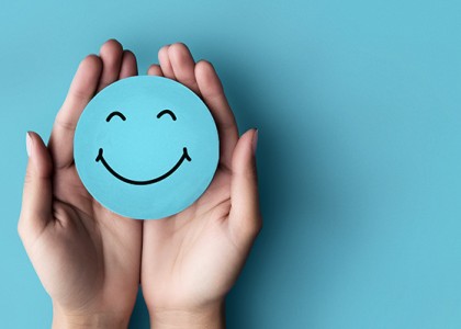 An image of hand against a blue background holding a blue circle smiley face