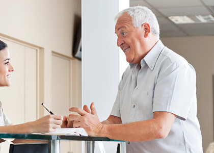 A front of desk person discussing paperwork with an older male patient