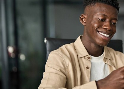 A young man smiles while looking at his cell phone.