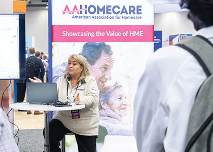 A speaker making a lecture at Medtrade in front of an AAHomecare sign