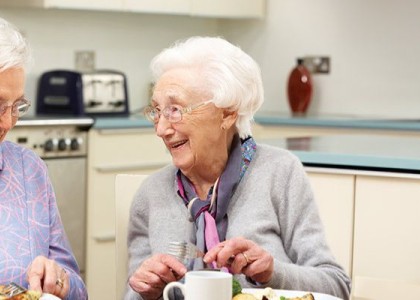 Two elderly women sit and laugh while enjoying their lunch.