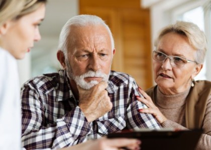 Husband and wife sit with a caregiver looking at a care plan