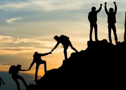 a group of people climbing up a mountain and helping each other reach the top