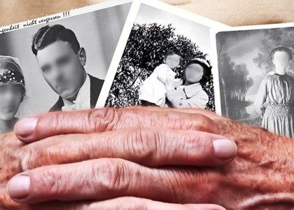 Two elderly hands hold old photographs with the faces blurred out.