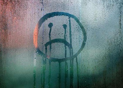 a frown face drawn on a window through condensation