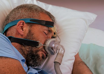 A man sleeps on a pillow with a sleep apnea mask on his face.