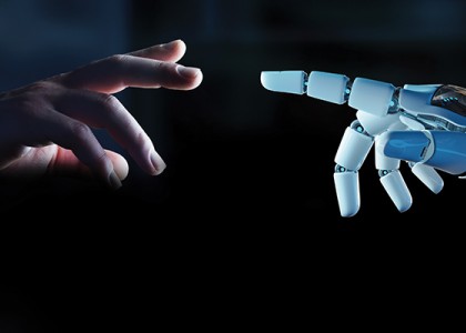 A human hand reaching out to a robot hand on a dark background