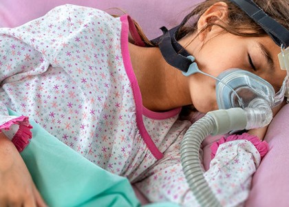 A girl lays sleeping with a CPAP machine on her face